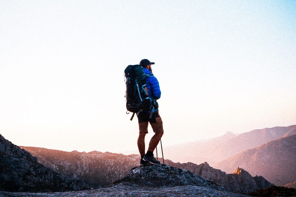 Deutsch: Ein Wanderer, der bei Sonnenaufgang auf einem Berg in die Ferne schaut – ein Moment der Ruhe und des Abenteuers in der Natur. Englisch: A hiker gazing into the distance from a mountain at sunrise – a moment of peace and adventure in nature.